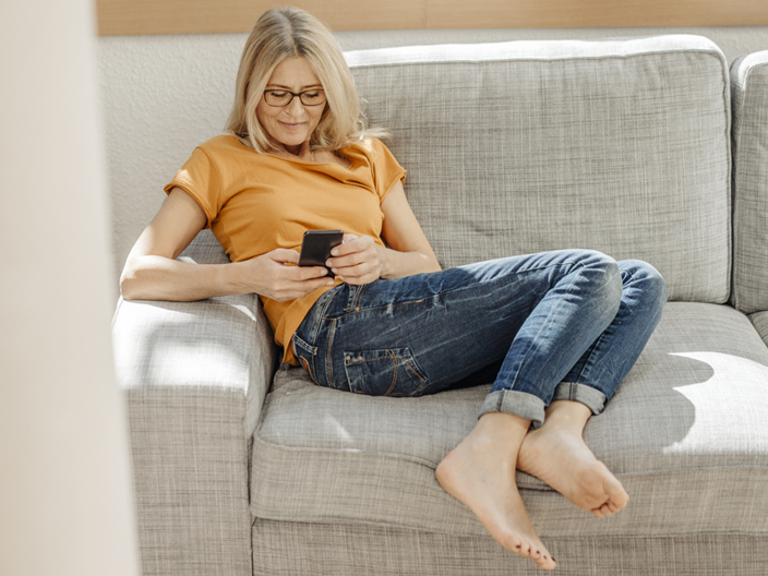 Woman with glasses checkin her phone on a sofa